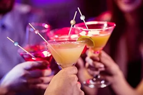 Colorful cocktails garnished with bamboo picks held in a toast