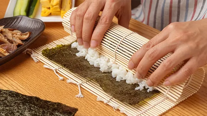 Hände rollen Sushi mit Bambus-Sushi-Matten für die hausgemachte Zubereitung