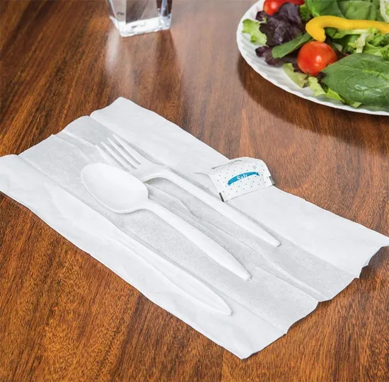 Cubiertos blancos de peso medio envueltos con servilleta sobre la mesa.