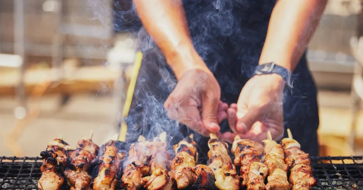 Person grilling skewers over open flame grill Person grilling skewers over open flame grill