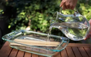 Pouring water to soak skewers in glass tray