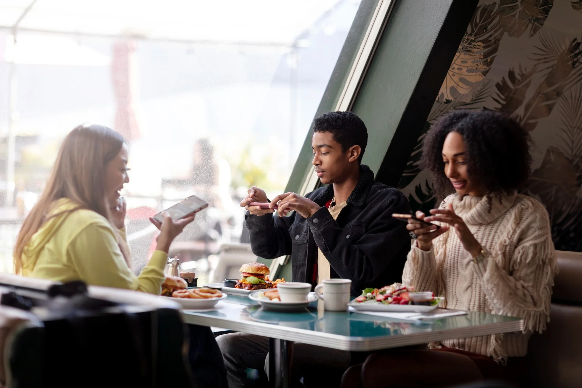 Três amigos tirando fotos de comida em uma mesa de lanchonete. Três amigos tirando fotos de comida em uma mesa de lanchonete.