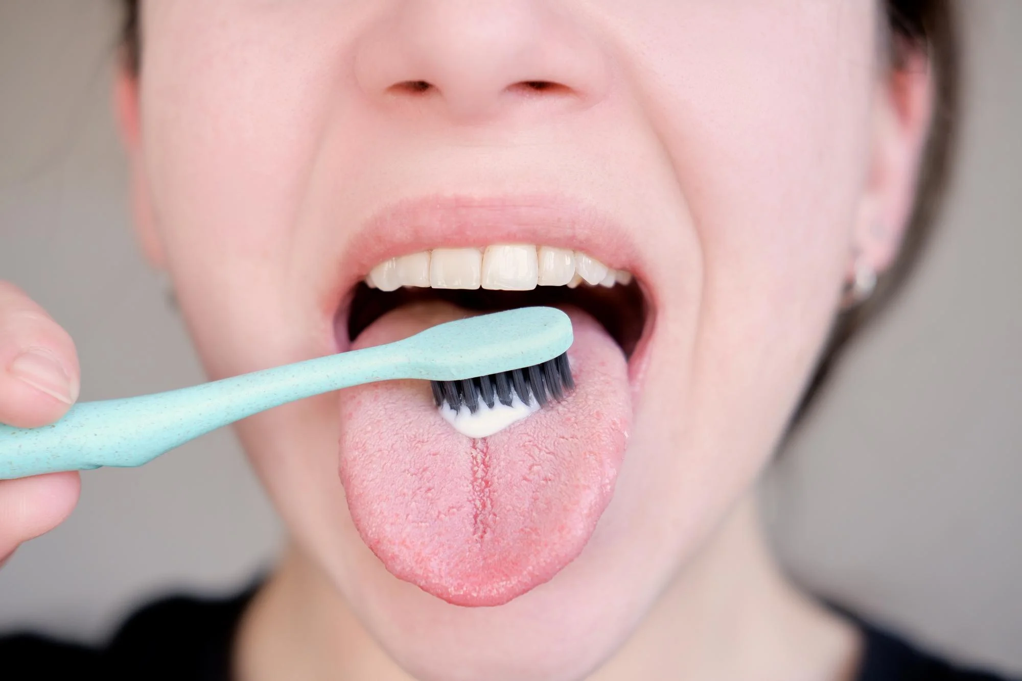 Woman brushing her tongue with a blue toothbrush Woman brushing her tongue with a blue toothbrush