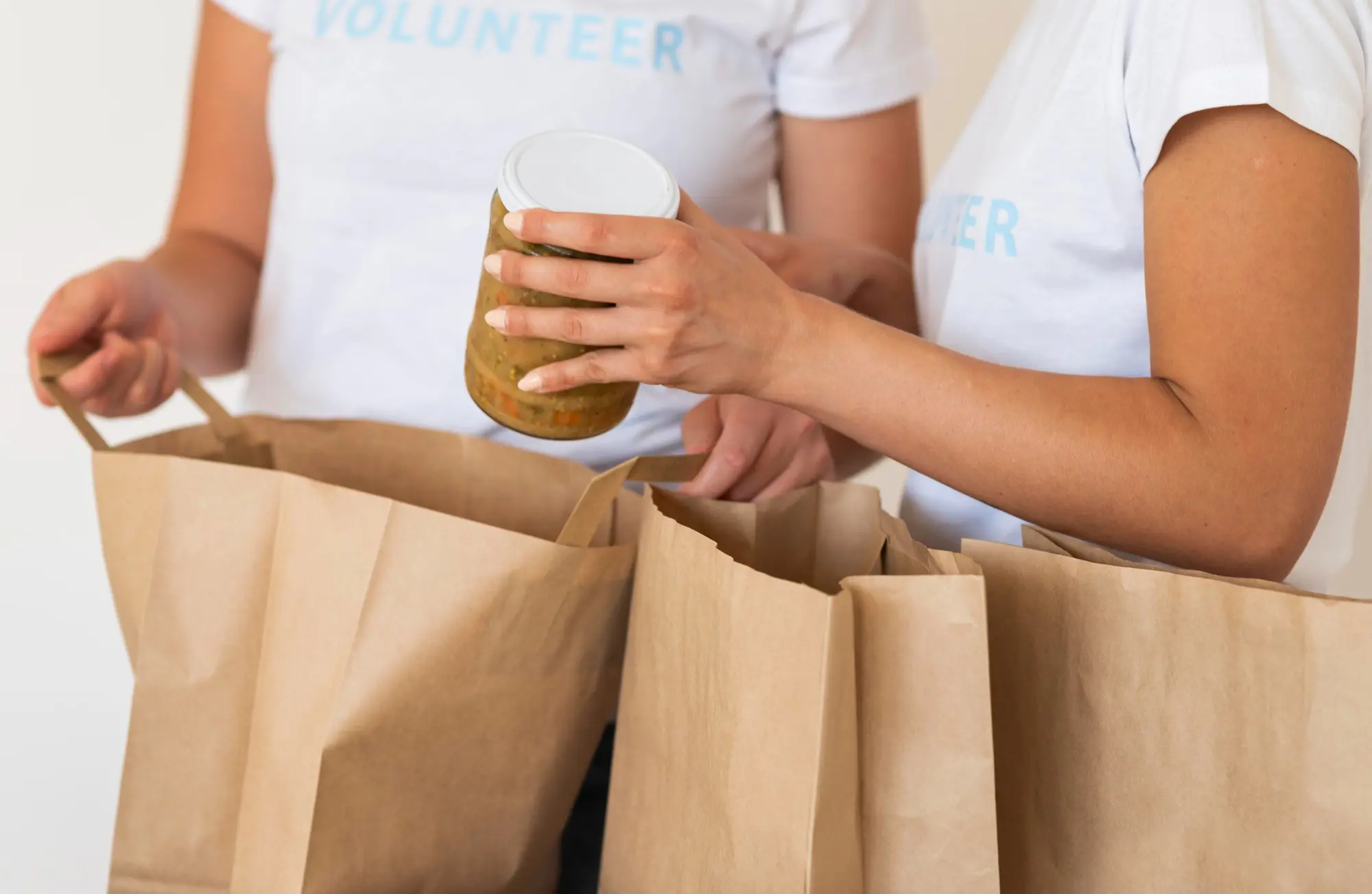 Voluntários embalando alimentos usando sacolas de papel kraft com alças planas.